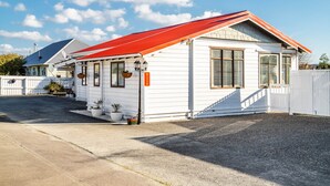 A white mobile home with a red roof, a front porch, and a gravel driveway. - Deluxe Three Bedroom Villa (Upper Hutt)