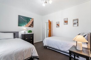Une chambre d’hôtel avec deux lits, une table de chevet, une lampe, une commode et une porte.