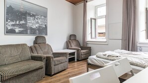 Een hotelkamer met een bed, een slaapbank, twee fauteuils, een tafeltje en een groot raam.