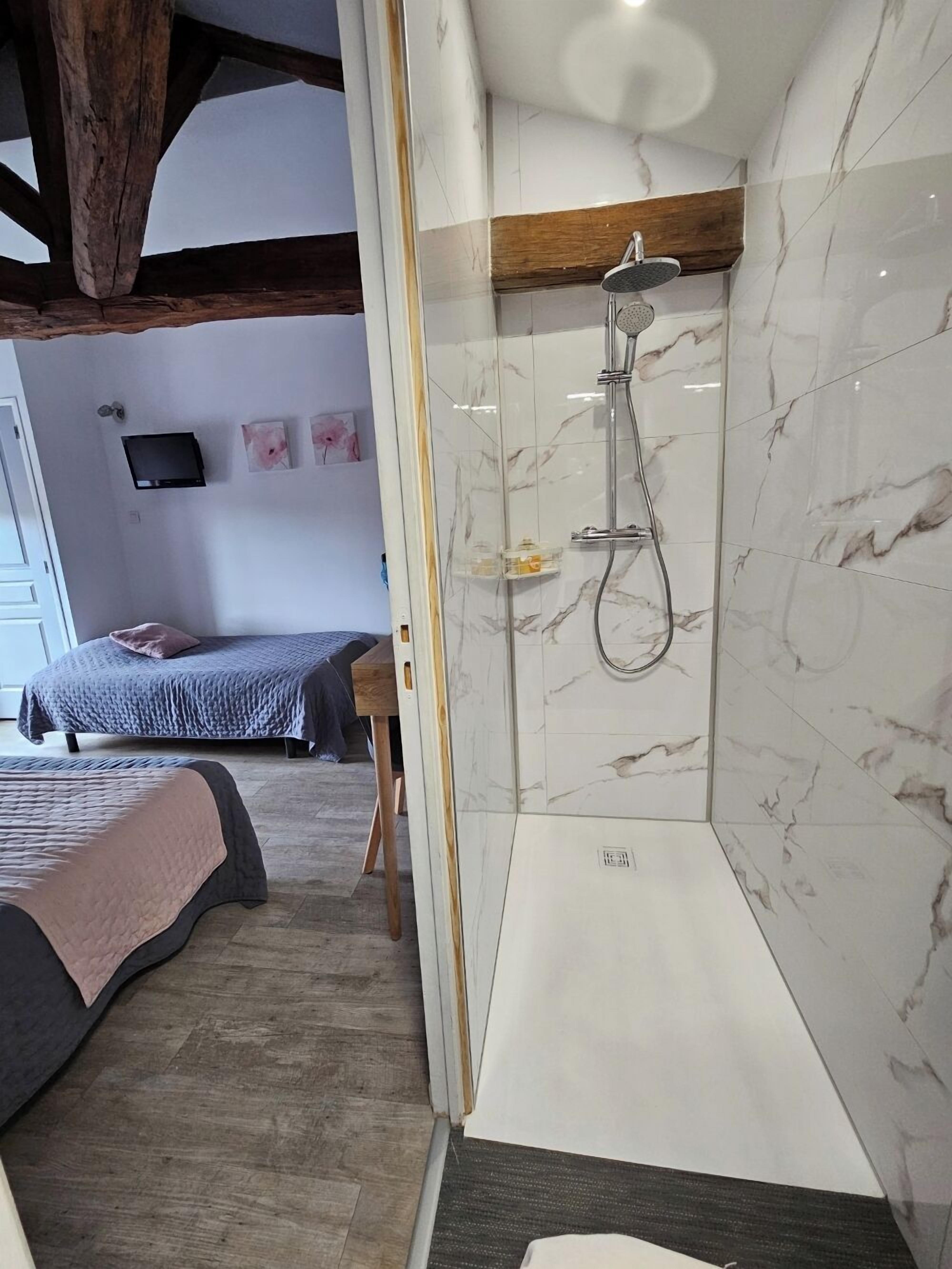 A modern bathroom with a glass-enclosed shower, marble walls, and a wooden ceiling beam.
