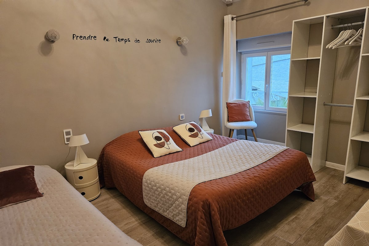 A bedroom with a large bed, a chair, a wardrobe, and a window.