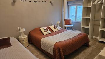 A bedroom with a large bed, a chair, a wardrobe, and a window.