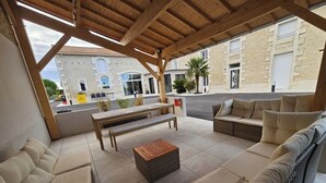 A covered outdoor seating area with a wooden bench, sofa, and a small table. - A la Gloriette Futuroscope (Neuville-de-Poitou)