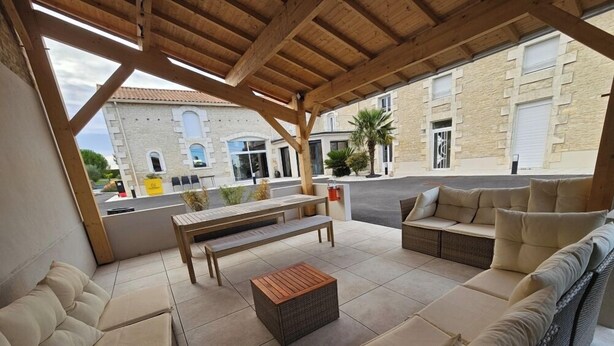 A covered outdoor seating area with a wooden bench, sofa, and a small table.