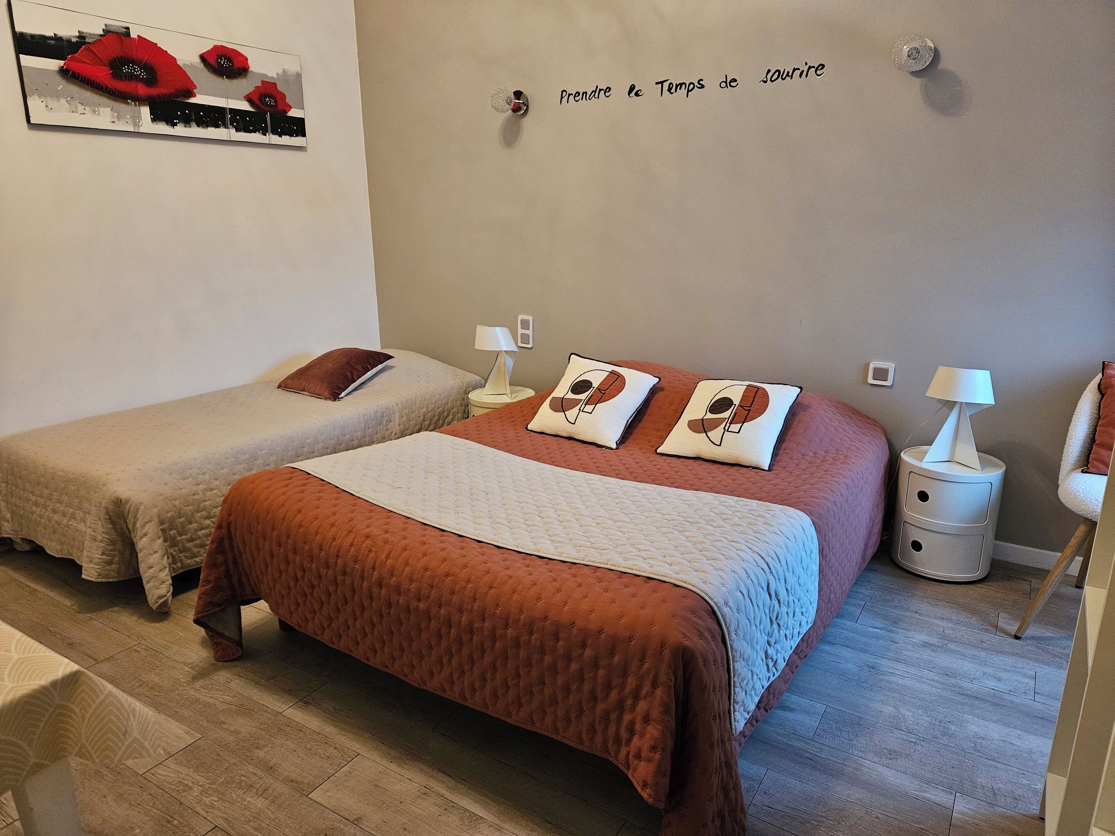 A bedroom with two single beds, a large bed with a brown bedspread, bedside tables with lamps, and a wall-mounted mirror.
