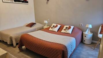 A bedroom with two single beds, a large bed with a brown bedspread, bedside tables with lamps, and a wall-mounted mirror.