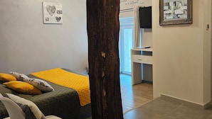 A modern bedroom with a large wooden beam ceiling, a bed with a yellow blanket, a chair, and a desk with a mirror. - A la Gloriette Futuroscope (Neuville-de-Poitou)