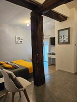Quarto moderno com teto alto de vigas de madeira, uma cama com manta amarela, uma cadeira e uma escrivaninha com espelho.