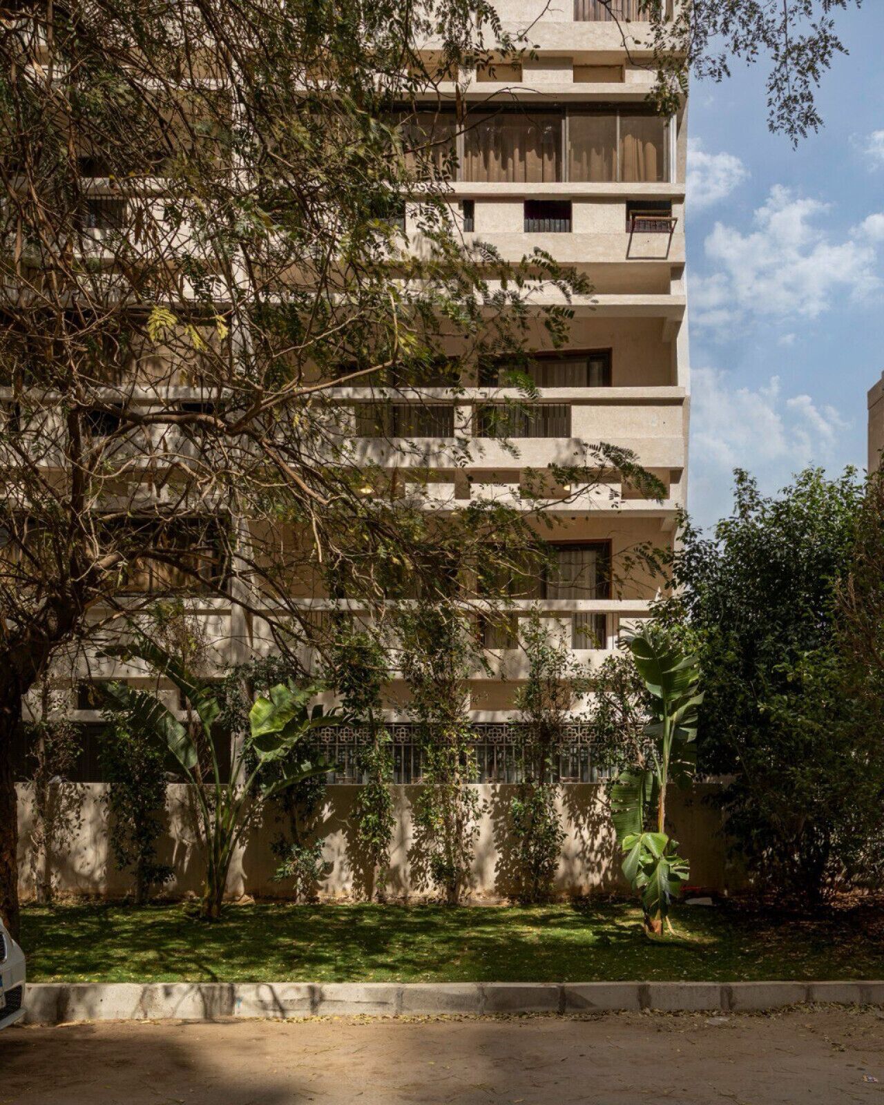 A multi-story building with balconies, surrounded by trees and greenery.