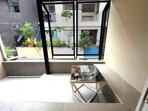 Un balcón con una mesa de vidrio, barandilla metálica y vistas de un edificio con varias ventanas y balcones.