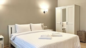 A neatly made bed with white linens and towels, a white wardrobe, and a wall-mounted light fixture. - Large Studio with Kitchen – 50m from Jomtien Beach (Muang Pattaya)