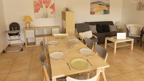 A dining area with a wooden table set for four, a high chair, and a sofa in the background.
