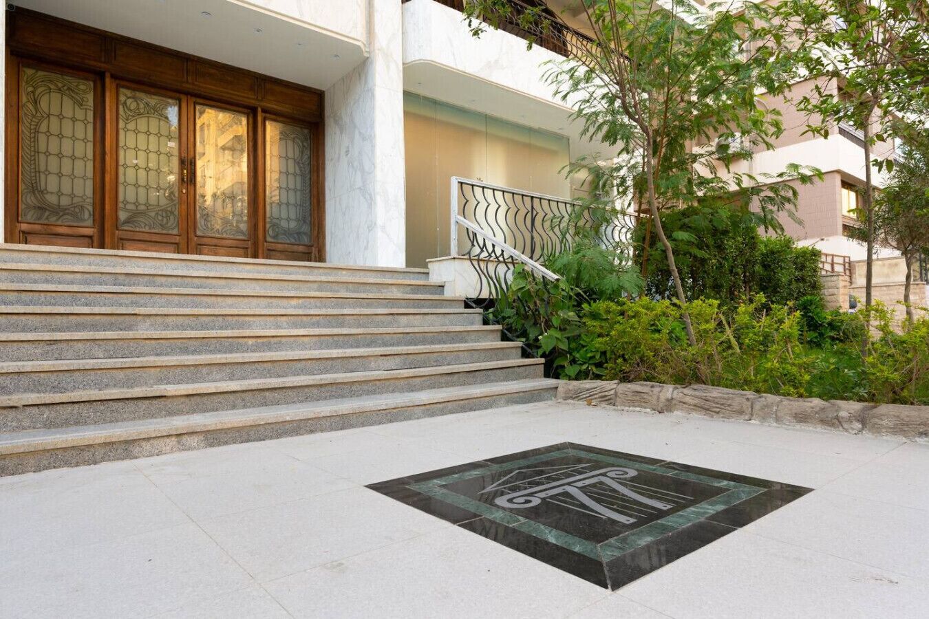 Une entrée d’immeuble avec un escalier en pierre menant à une porte en bois dotée de panneaux de verre.