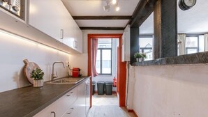 Een smalle keuken met witte kasten, een donker aanrecht en een raam met rode rand.