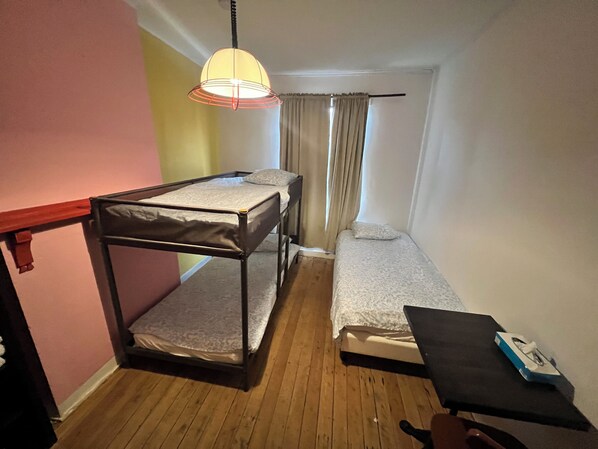 A small, compact room with a bunk bed, a desk, and a hanging lamp.