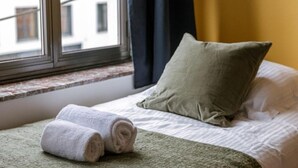 Een keurig opgemaakt bed met een groene deken en twee opgerolde witte handdoeken.