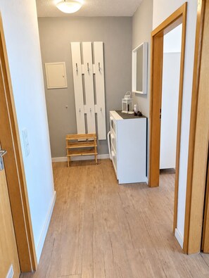 Un couloir avec un banc en bois, une armoire blanche et un miroir au mur.