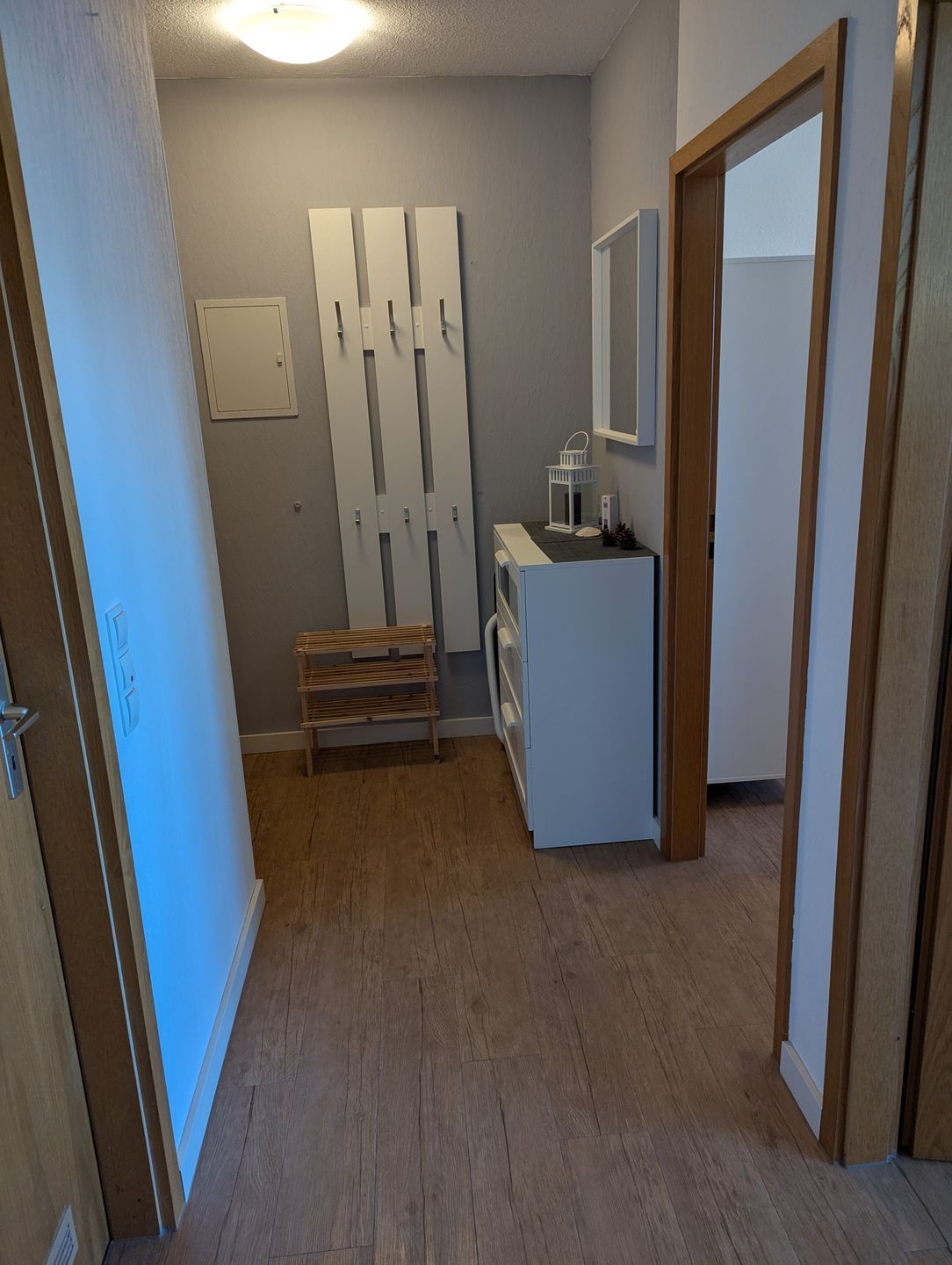 Ein schmaler Korridor mit einer hölzernen Bank, einem kleinen Tisch mit einer Laterne und einem weißen Schrank.