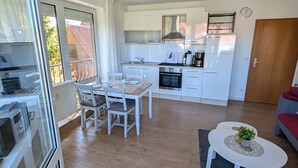 Una cucina compatta con mobili bianchi, un'area pranzo con tavolo e sedie, un piccolo tavolino da caffè bianco e un divano rosso.