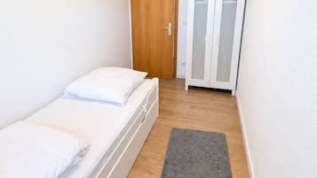 Ein kleines, sauberes Zimmer mit einem Bett, einem Kleiderschrank und einer Tür.