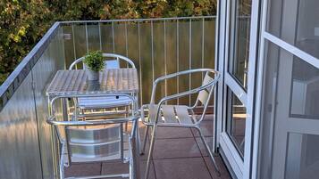 Ein Balkon mit einem Metalltisch und -stühlen, einem Blumentopf und Blick auf Bäume.