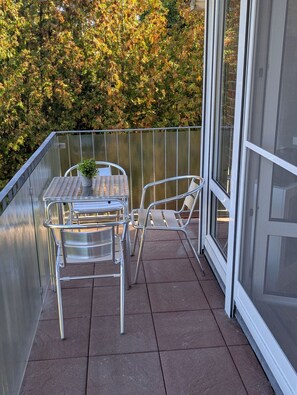 A balcony with a metal table and chairs, a potted plant, and a view of trees. - Comfortable vacation rental near the beach at Nige Ooge 9 with a balcony - House Nige Ooge (Cuxhaven)
