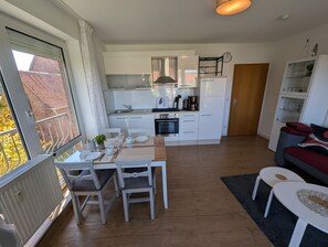 Una cocina moderna con armarios blancos, una mesa de comedor con sillas, un refrigerador pequeño y un reloj en la pared.