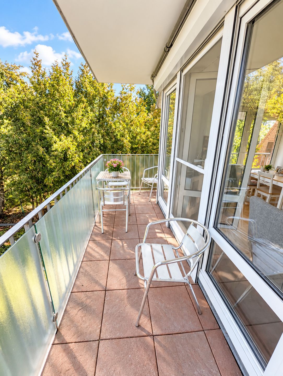 Ein Balkon mit Tisch und Stühlen, einem Blumentopf und Blick auf Bäume.