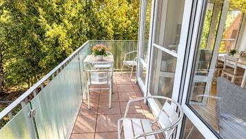 Ein Balkon mit Tisch und Stühlen, einem Blumentopf und Blick auf Bäume.