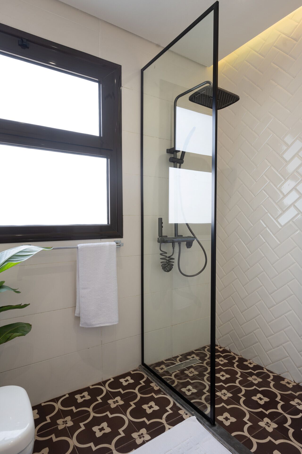 Une salle de bain avec une douche à parois de verre, des toilettes blanches et des carreaux de sol à motifs.
