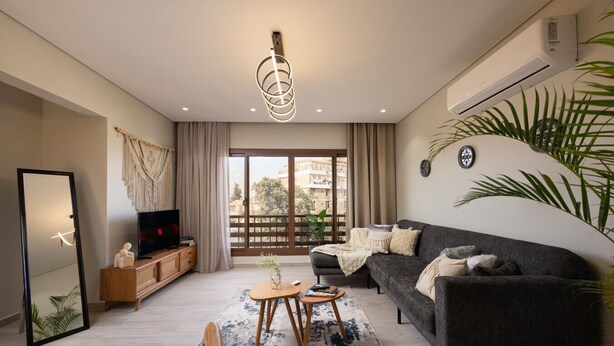 A modern living room with a sofa, TV, and a large window. - Degla by Spacey (#37) |1BR in Maadi (Cairo)