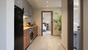 A modern kitchen with a washing machine, a refrigerator, and a countertop with fruits and a coffee maker. - Degla by Spacey (#37) |1BR in Maadi (Cairo)