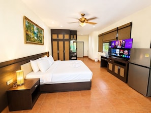 A hotel room with a bed, a desk with a computer, a television, and a refrigerator. - Relax Corner Jomtien – Spacious Studio with Balcony (Muang Pattaya)