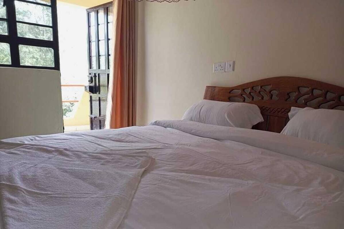 A hotel room with a large bed, a wooden headboard, and a window with curtains.