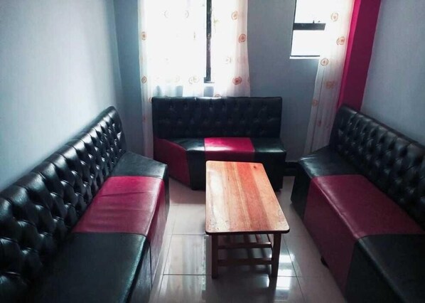 A seating area with black leather sofas and a wooden table. - Pennjoki Resort (Kakamega)