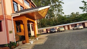 A building with a covered porch, a gravel driveway, and parked cars. - Pennjoki Resort (Kakamega)