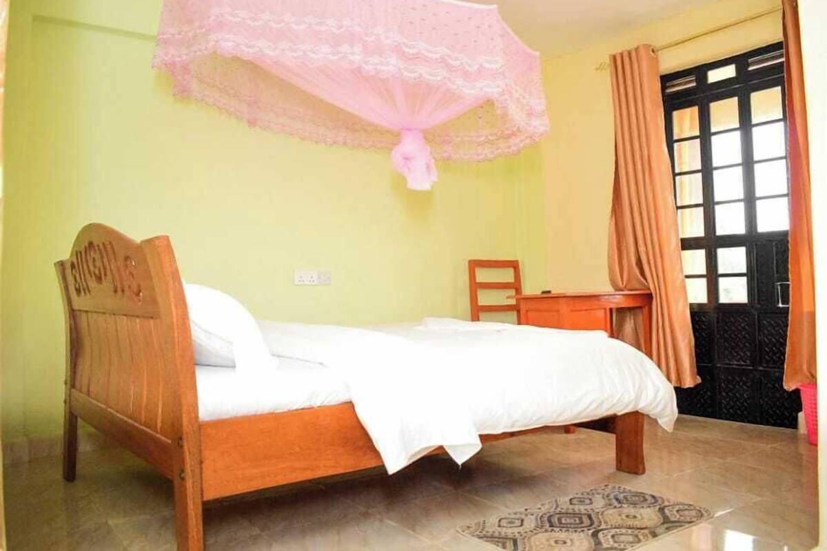 A bedroom with a wooden bed, a desk, a chair, a window with curtains, and a patterned rug.