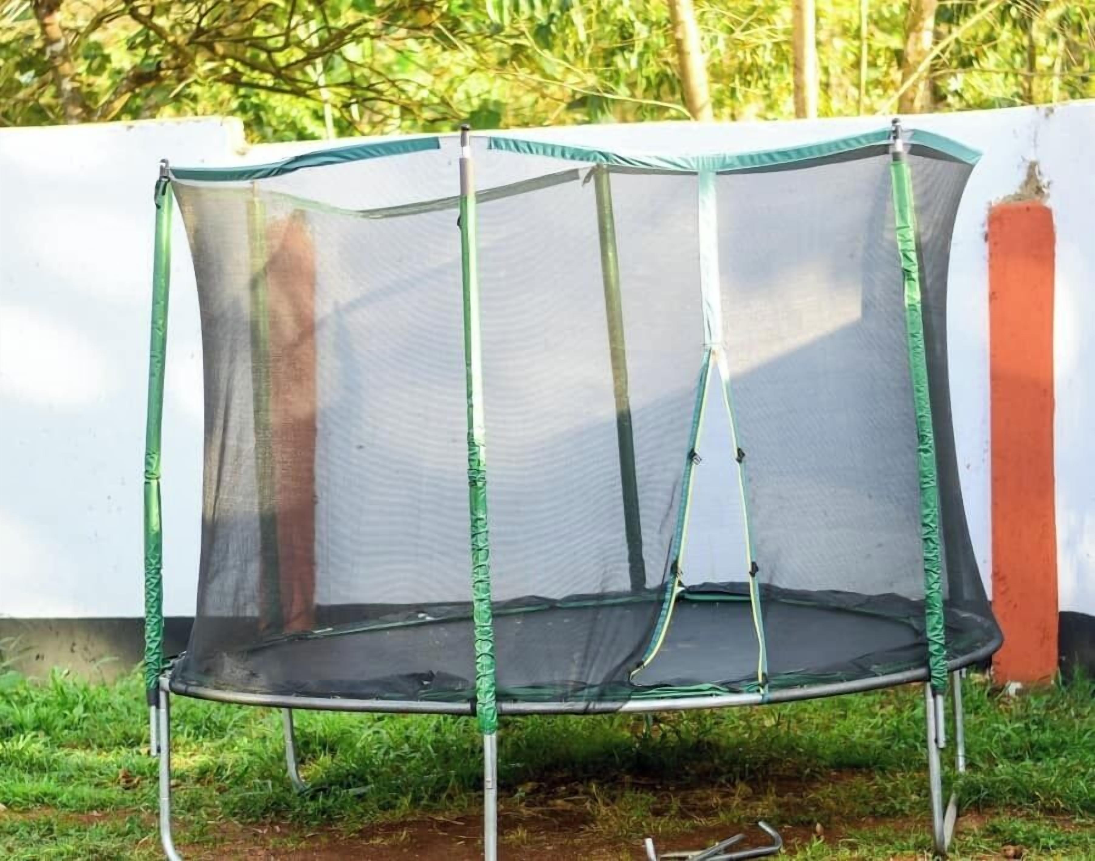 Un trampoline doté d’un filet de sécurité, entouré d’un mur blanc et d’une pelouse.