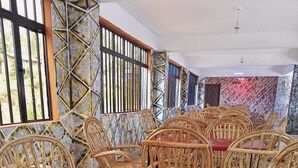 A dining area with wicker chairs and a red table, featuring a geometric patterned wall and a window with vertical bars. - Pennjoki Resort (Kakamega)