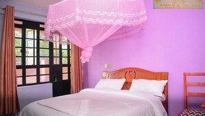 A bedroom with a bed, a wooden headboard, a pink mosquito net, and a sign on the wall. - Pennjoki Resort (Kakamega)