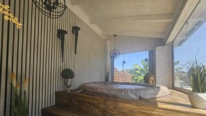 Una camera da letto moderna con un letto a piattaforma in legno, una pianta in vaso e vista sull'esterno.