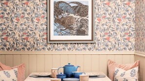 Una habitación con papel tapiz estampado, una obra de arte enmarcada y una mesa dispuesta con vajilla azul y beige.