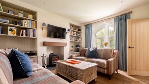 Una sala de estar acogedora con sofás a rayas, una mesa de centro de madera, una estantería y una chimenea.