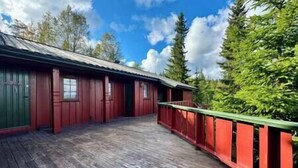 A red wooden building with a balcony, surrounded by trees and a clear sky.