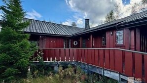 A red wooden building with a metal roof, surrounded by greenery and trees.