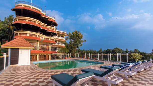 A hotel with a pool, lounge chairs, and a multi-story building with balconies. - Atreya Ayurveda & Yoga Beach Retreat  (Kovalam)
