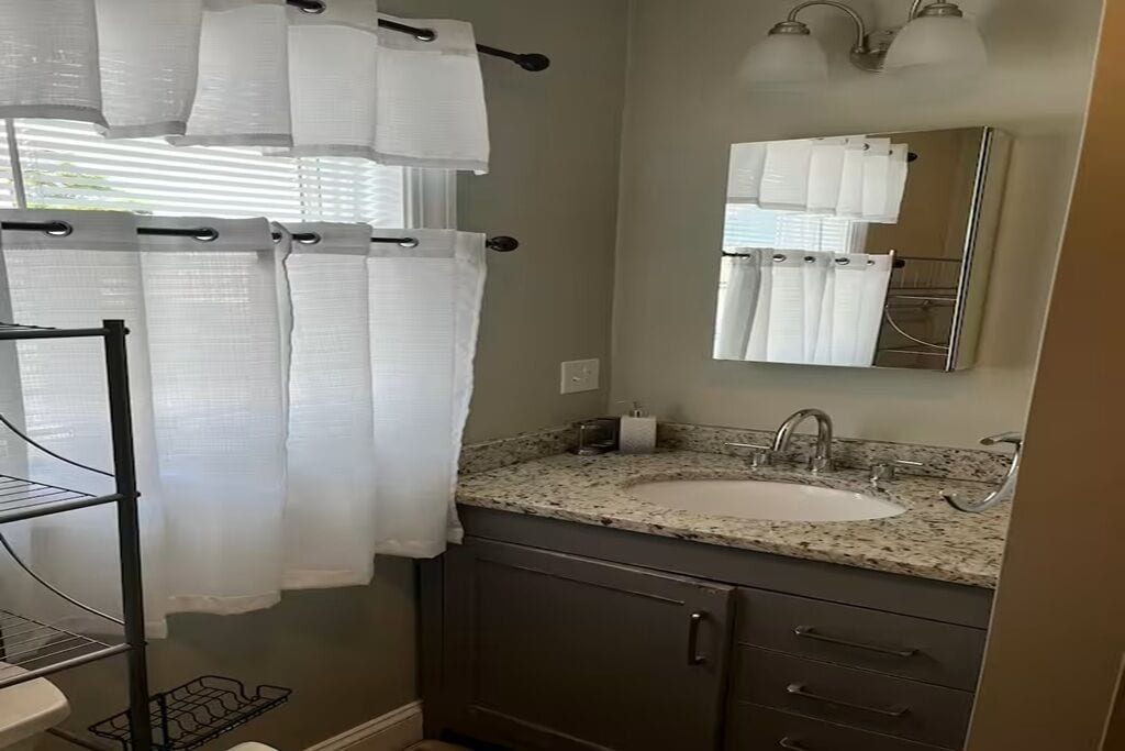 A bathroom with a sink, mirror, towel rack, and shower curtain.