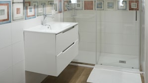A modern bathroom with a white vanity, a large mirror, a hairdryer, and a glass shower enclosure. - BlueB&B (Pagani)