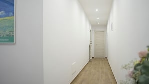 A narrow, well-lit hallway with a wooden floor, white walls, and a door at the end. - BlueB&B (Pagani)