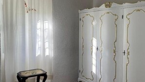 A room with a white wardrobe with gold trim, a small black table, and a sheer curtain with a floral pattern. - Crosa Rosella (Bardineto)